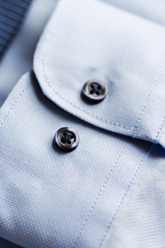 Dettaglio polsino di camicia azzurra con bottoni in madreperla scura