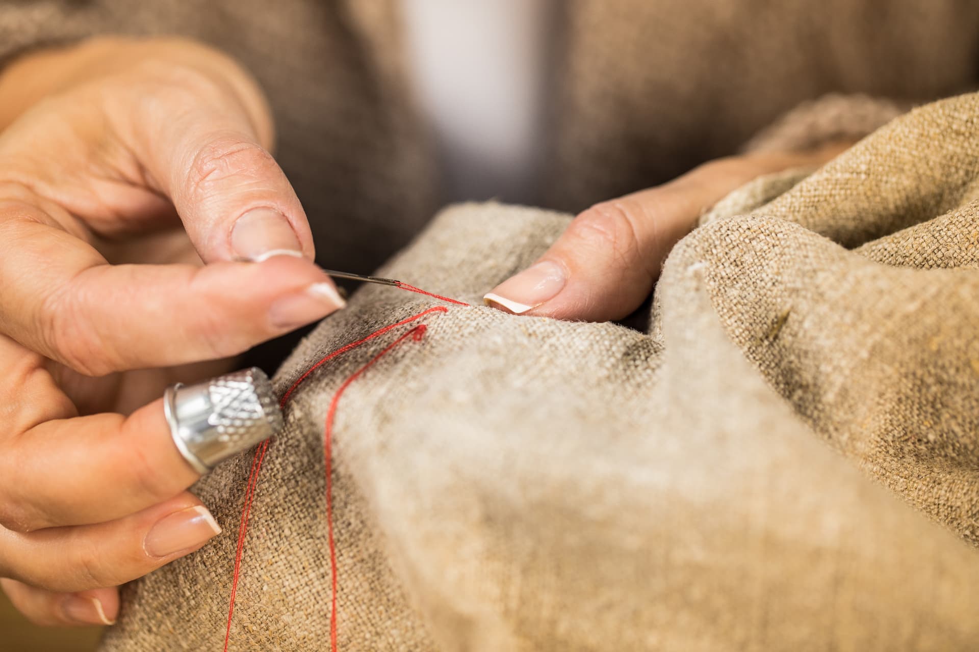 Mani di sarta che cuciono a mano un tessuto con ago, ditale e filo rosso