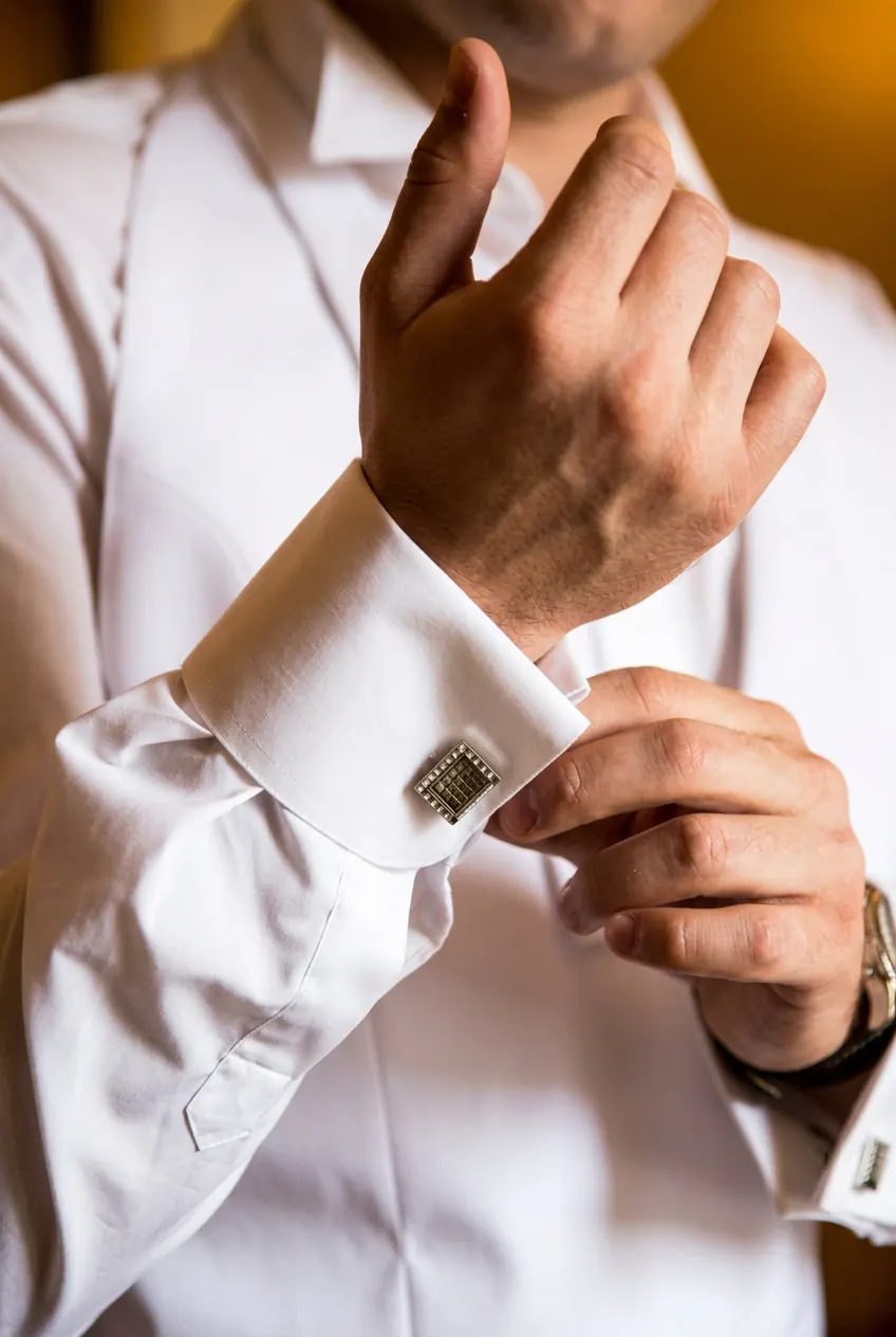 Dettaglio di un polsino gemelli con gemello in madreperla e metallo su camicia bianca su misura